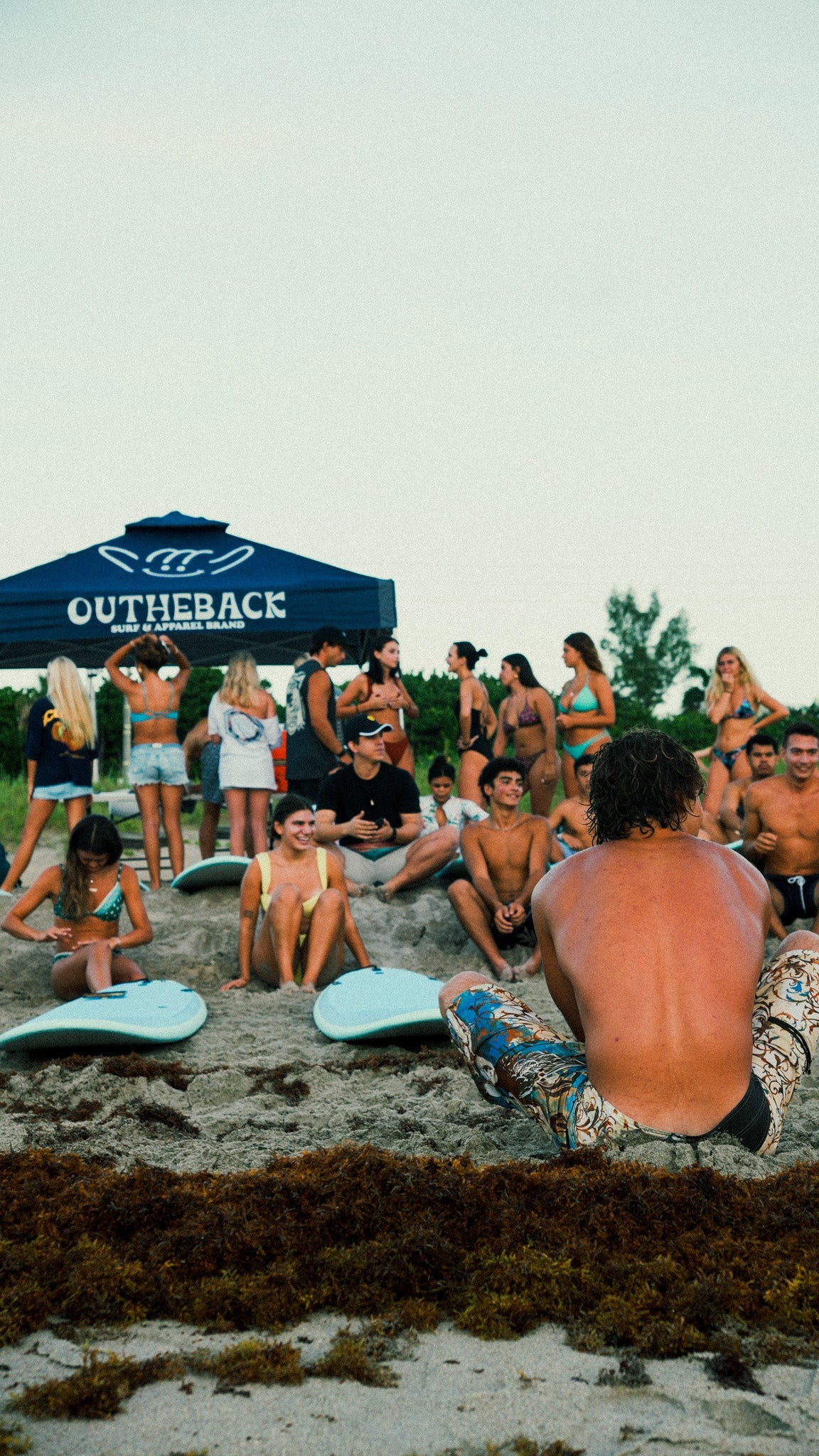 Group of people on a beach with 'Outheback' branded umbrella