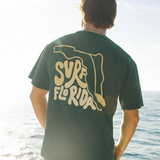 Person wearing a green t-shirt with 'Surf Florida' design by the ocean