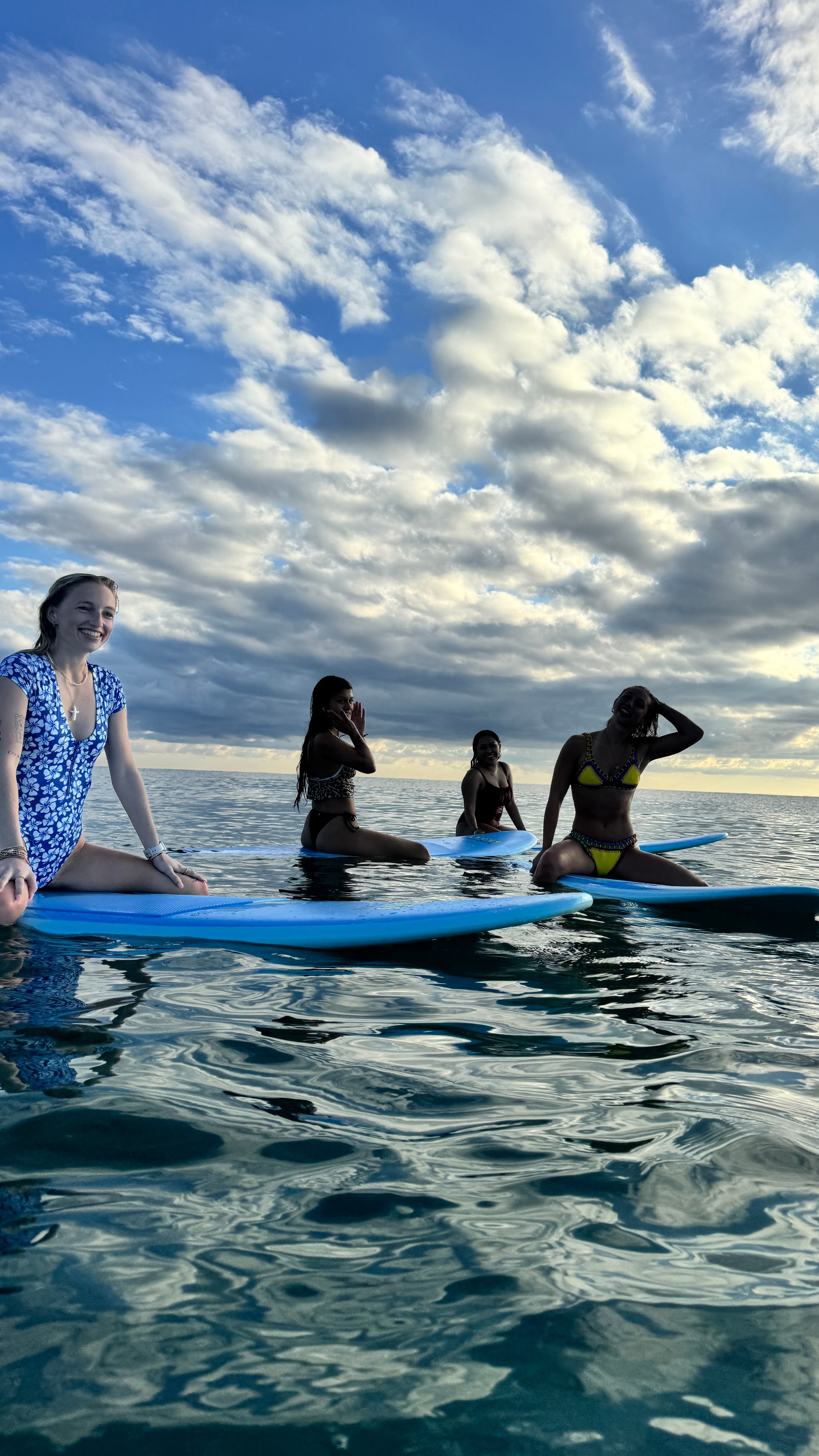 People on a beach with a blue surfboard, reflecting in the water.