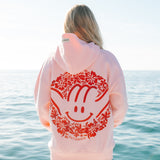 Person wearing a pink hoodie with a red design by the ocean