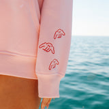 Pink sweatshirt with red designs on sleeves against a blue ocean background