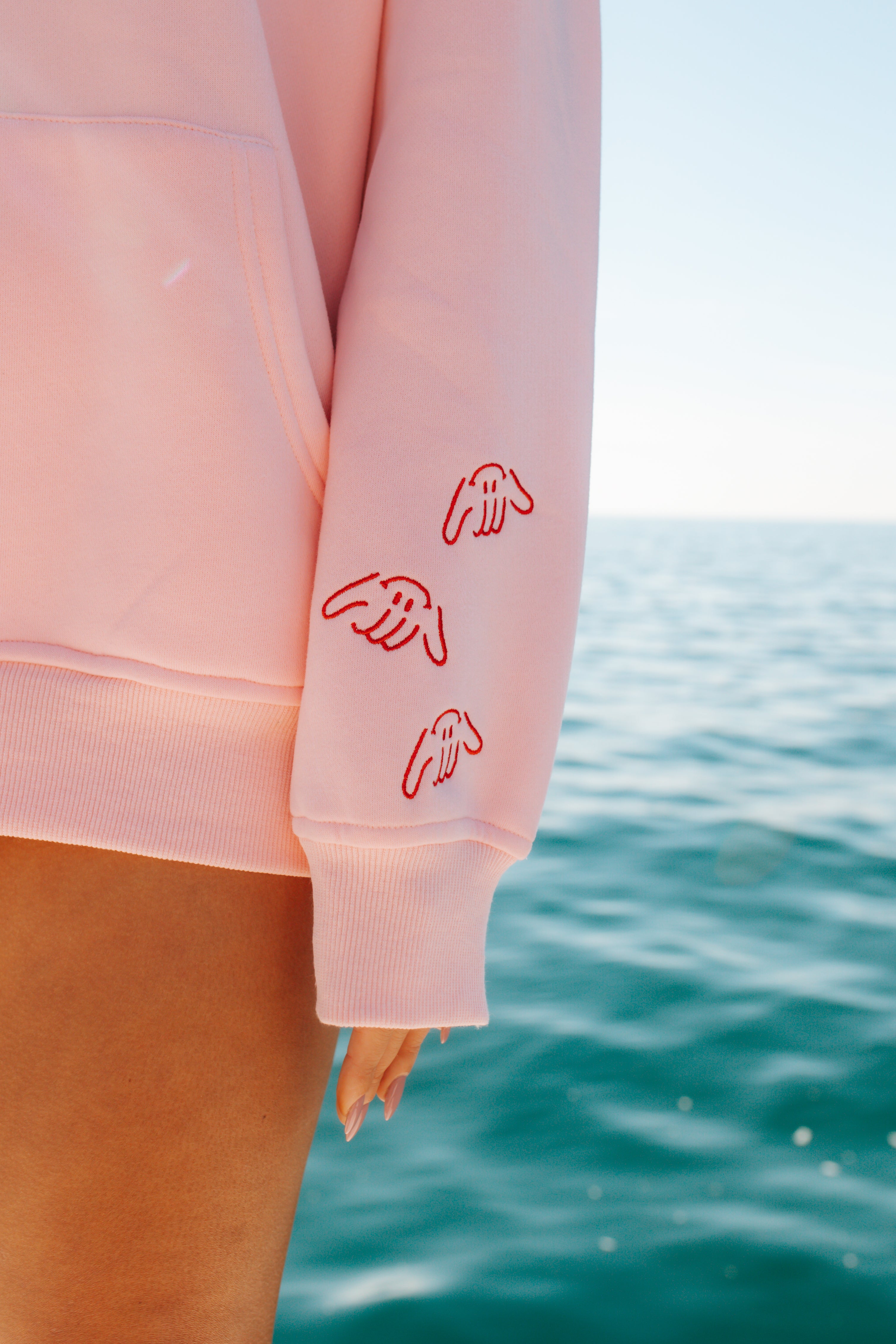 Pink sweatshirt with red designs on sleeves against a blue ocean background
