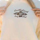 Beige hoodie with 'Outhouse Surf Club' logo worn by a person