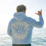Person wearing a light blue hoodie with a smiley face design by the ocean