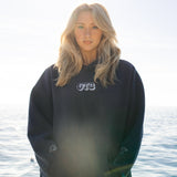 Person wearing a black hoodie with 'OTB' logo by water