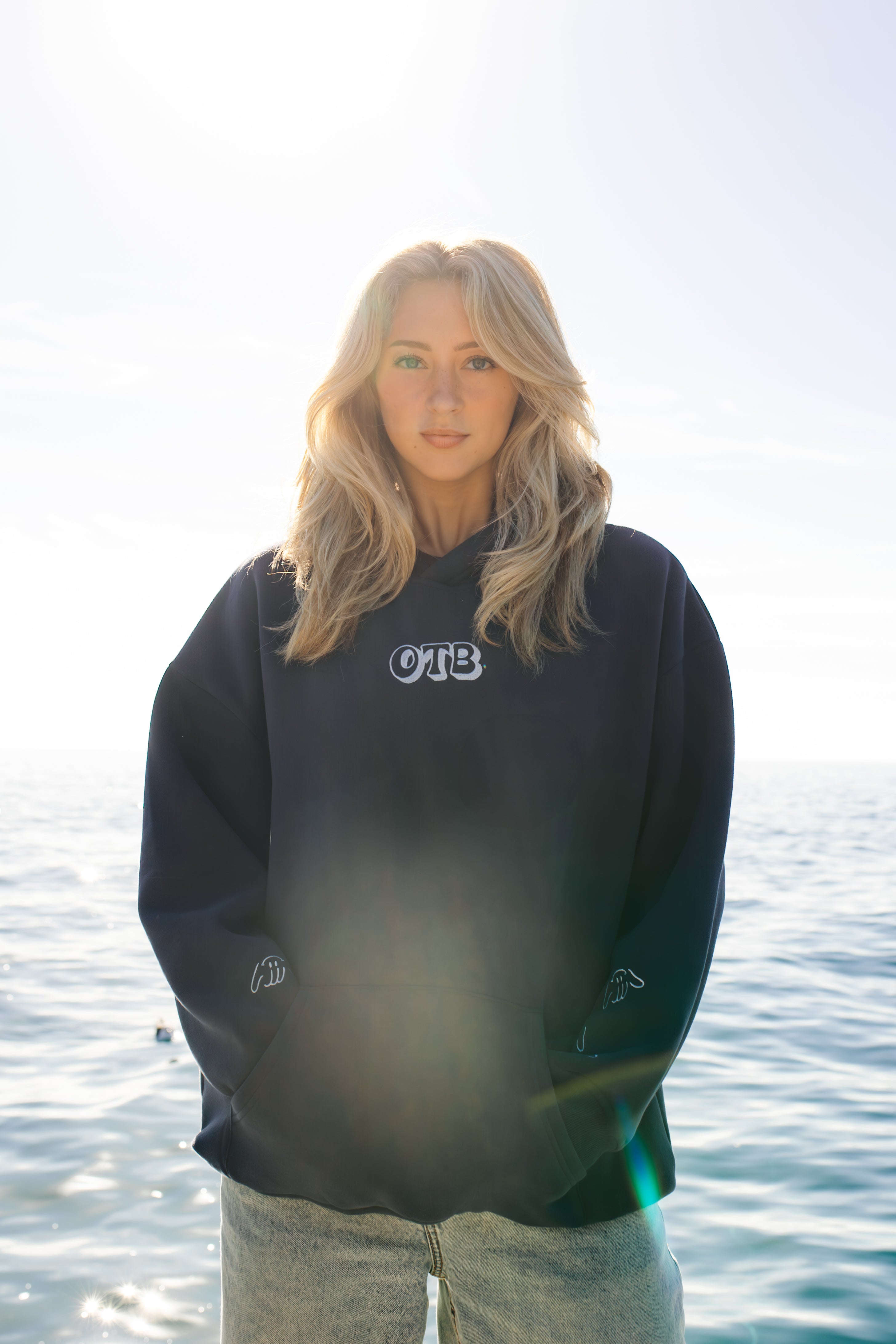 Person wearing a black hoodie with 'OTB' logo by water