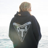 Person wearing a navy hoodie with a shark tooth logo by the water
