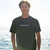 Person wearing a black 'Outback' t-shirt standing by the water.