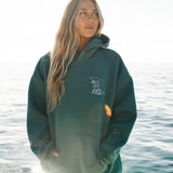Person wearing a green hoodie with a logo, standing by the water.