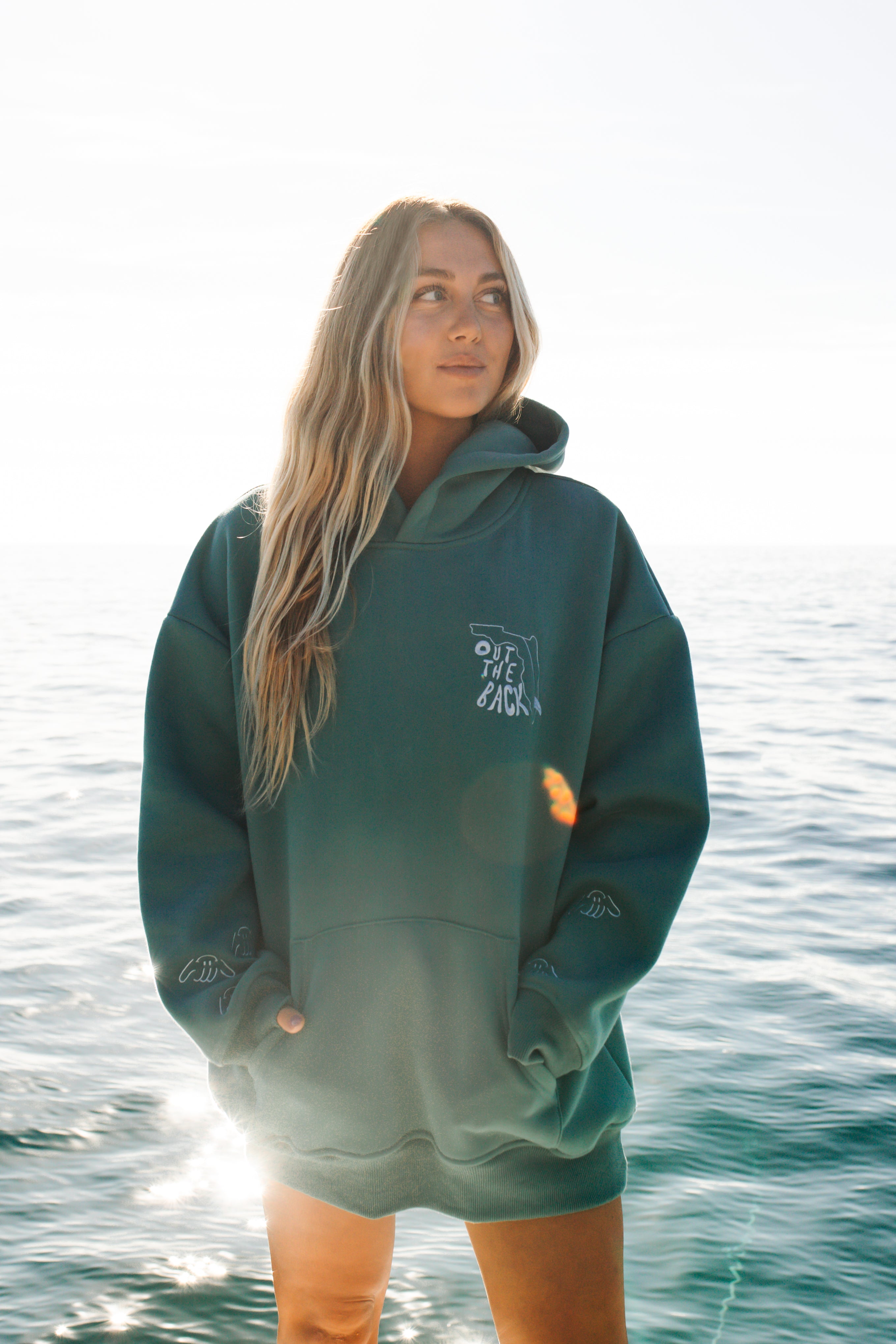 Person wearing a green hoodie with a logo, standing by the water.