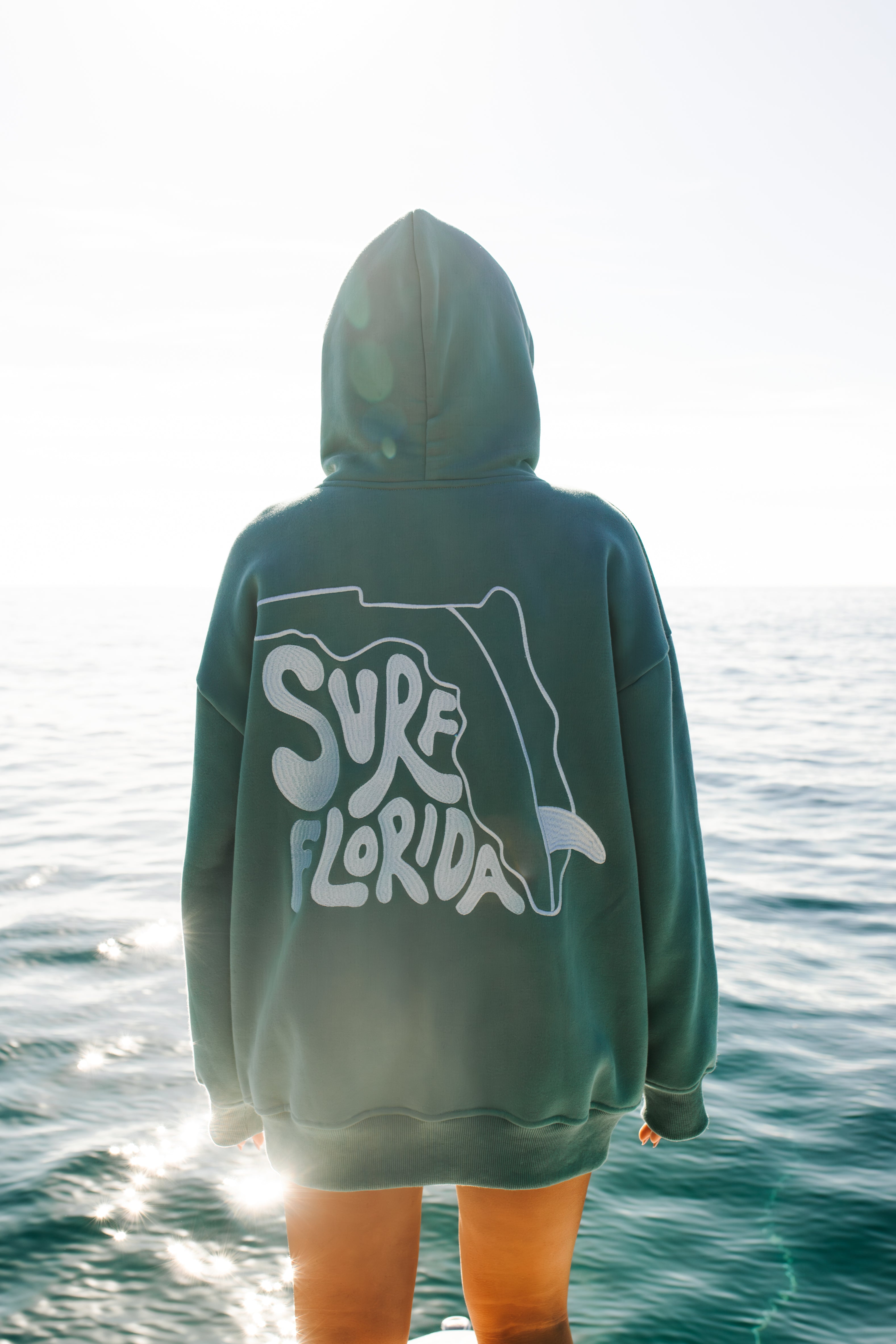Person wearing a hoodie with 'Surf Florida' text by the ocean