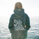 Person wearing a hoodie with 'Surf Florida' text standing on a beach.