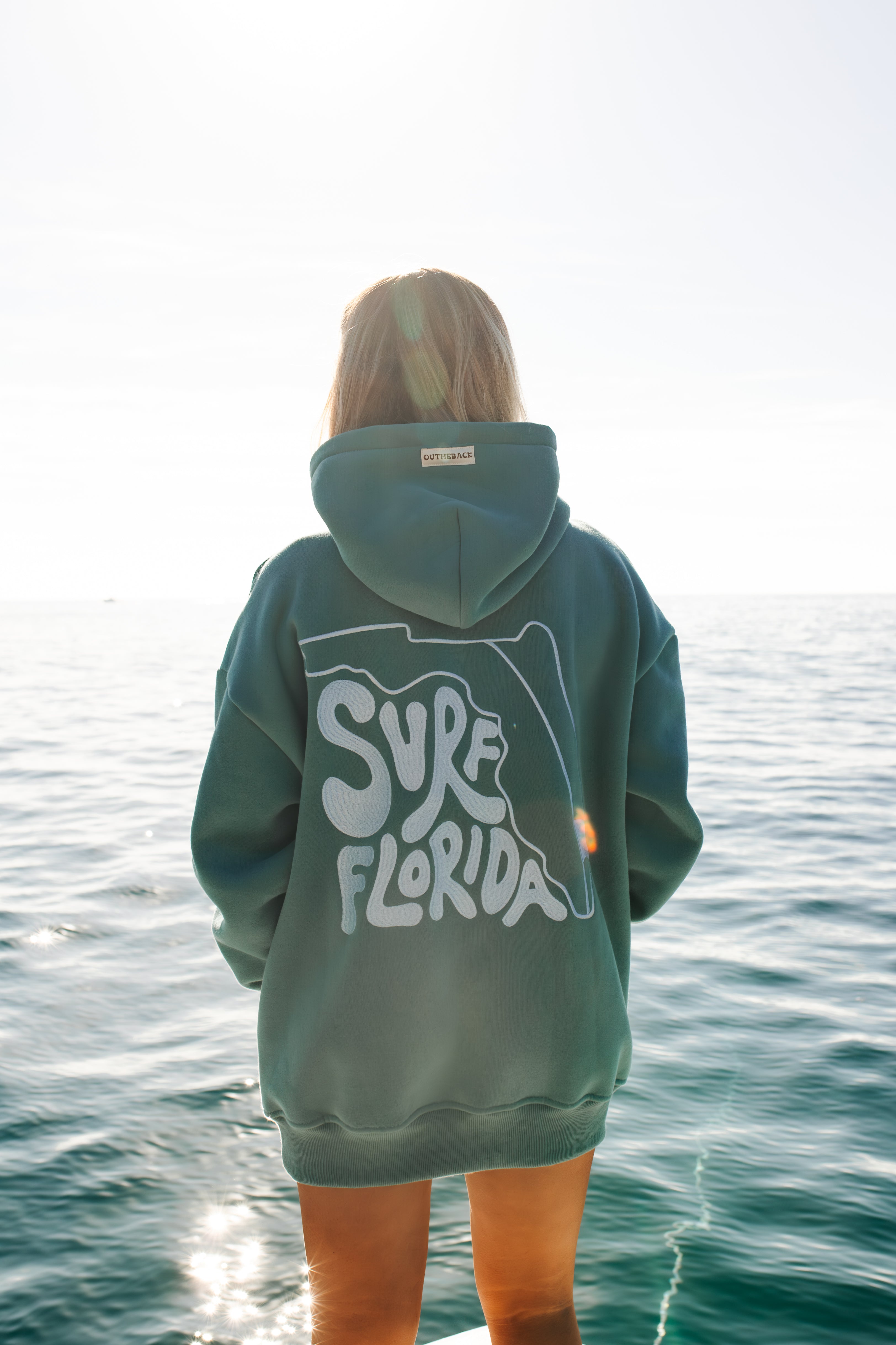Person wearing a hoodie with 'Surf Florida' text standing on a beach.