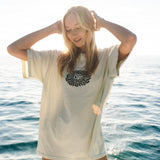 Woman on a boat wearing a light-colored shirt with a graphic design, with water in the background