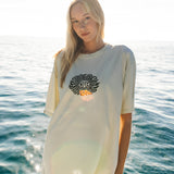 Woman wearing a white long-sleeve shirt with a logo on a boat with ocean in the background
