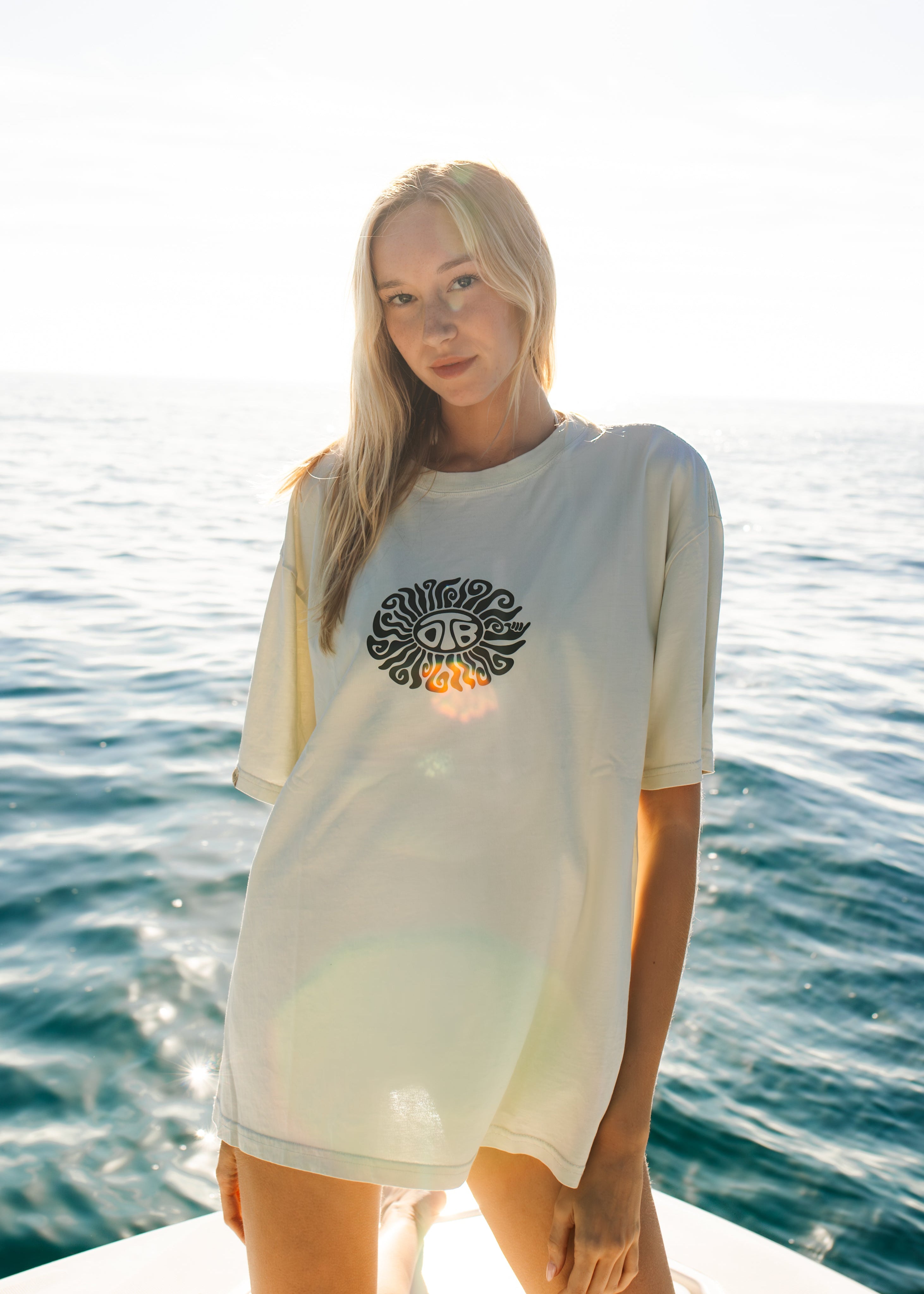 Woman wearing a white long-sleeve shirt with a logo on a boat with ocean in the background