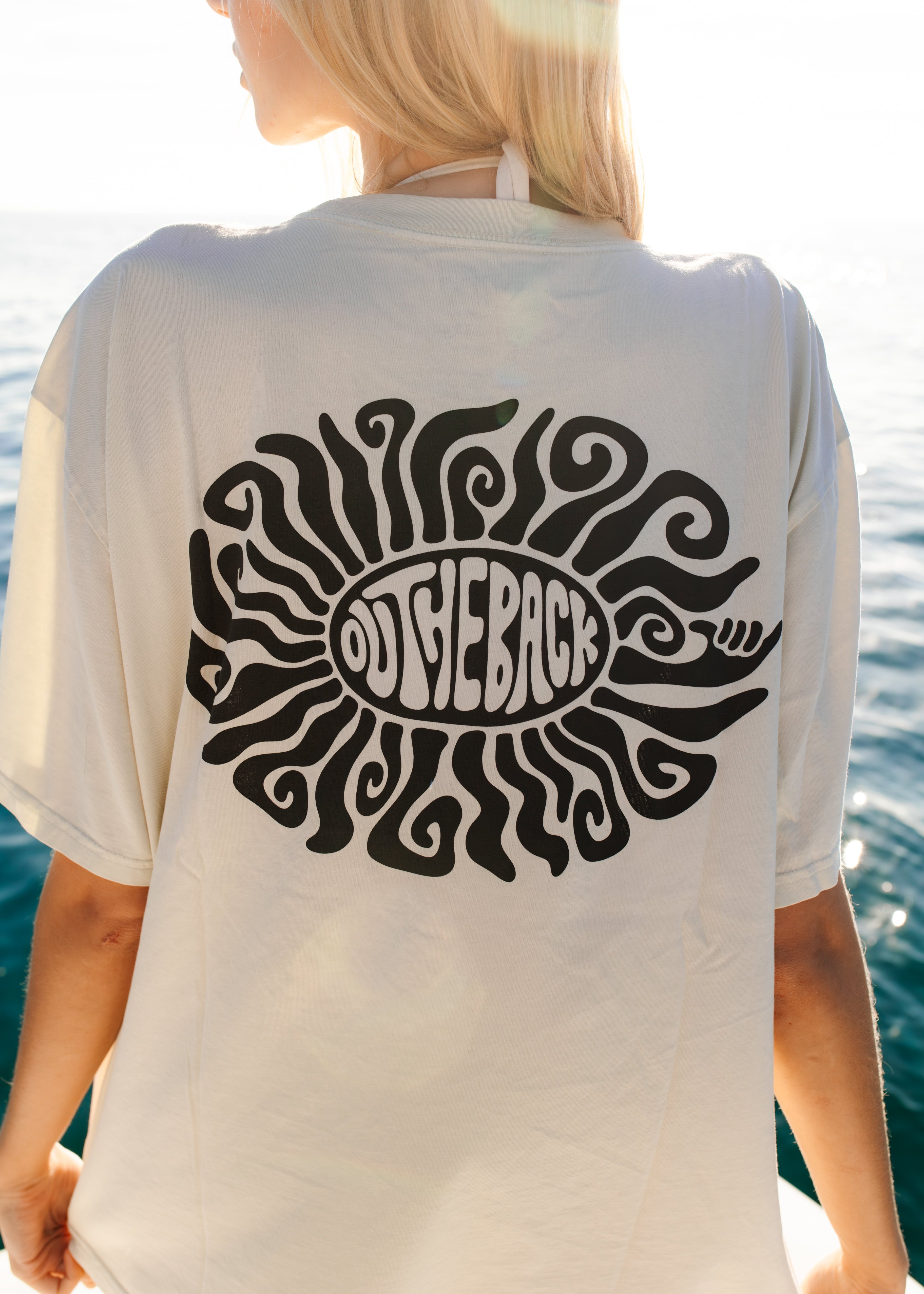 Person wearing a white t-shirt with a black graphic design by the water