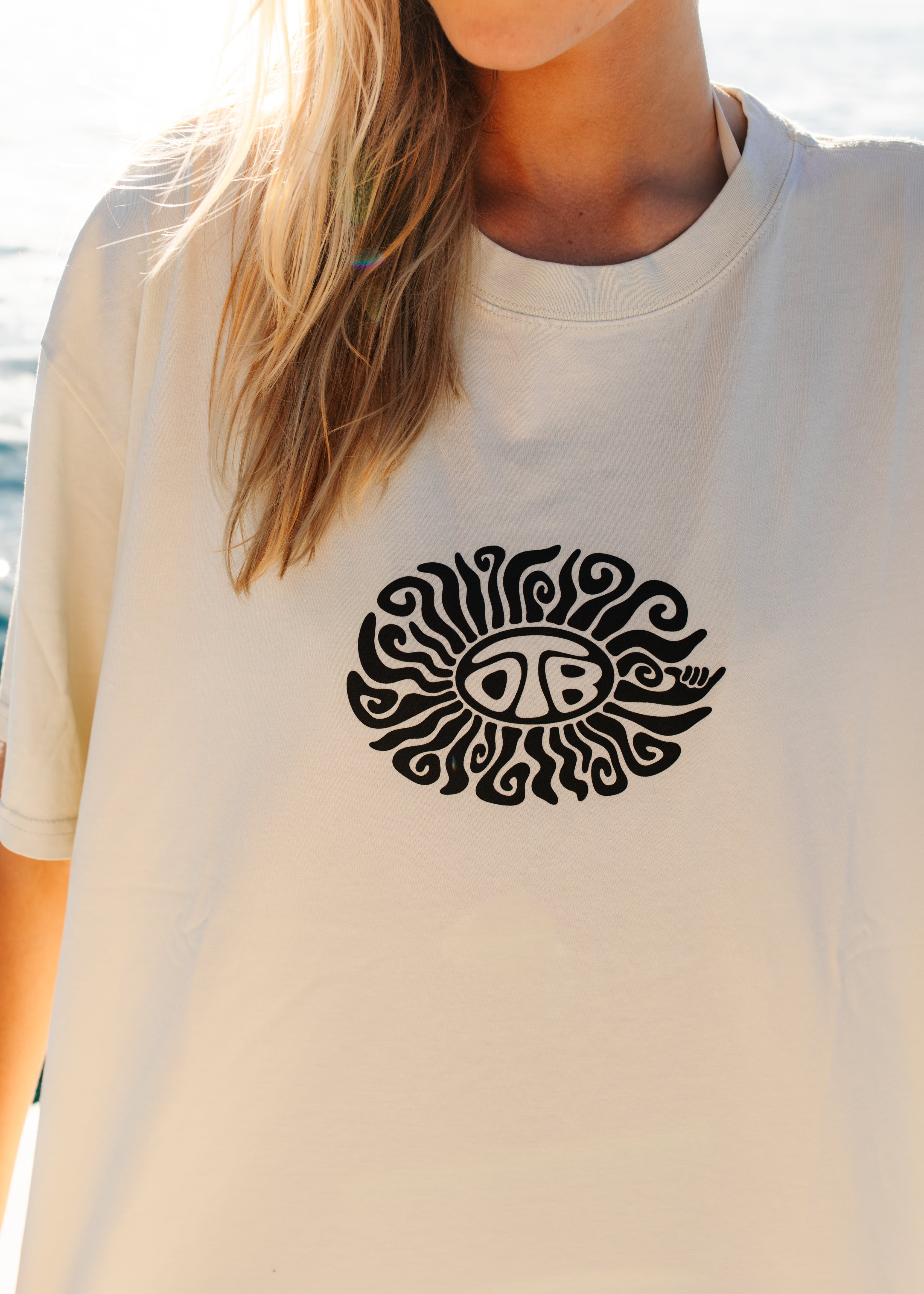 Person wearing a white t-shirt with a black sun design on a beach.