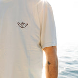 Person wearing a white t-shirt with a small logo, standing by water.