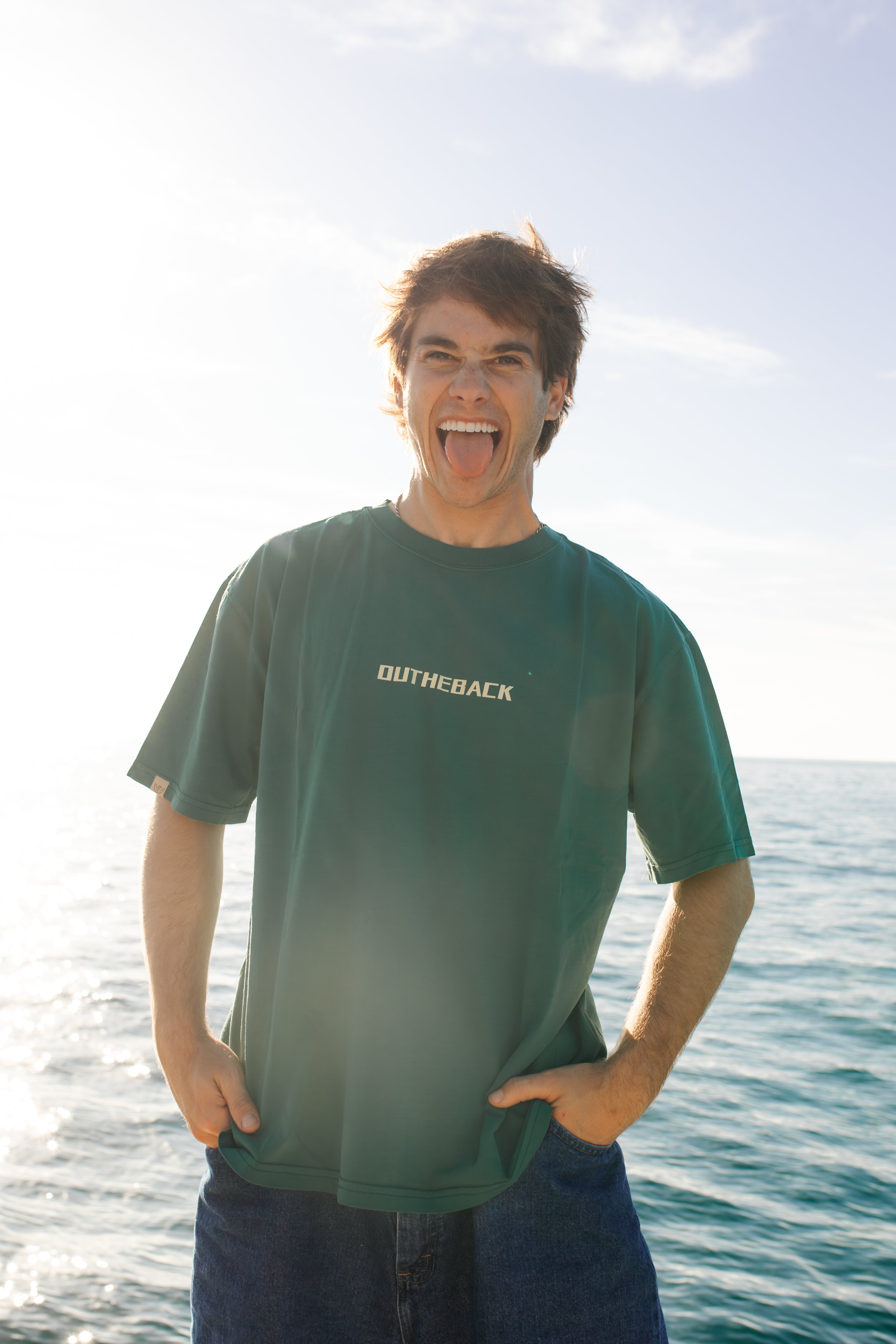 Person wearing a green t-shirt with 'Duthie Back' logo standing by the ocean.